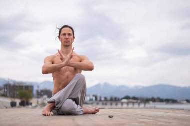 Beyaz bir adam, çıplak gövdesiyle deniz kıyısında wushu yapıyor.