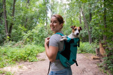 Beyaz bir kadın özel bir sırt çantasıyla köpek Jack Russell Terrier ile dışarı çıkıyor.
