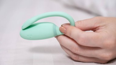 Beyaz çarşafta uzanırken elinde naneli vibratör tutan kadın.