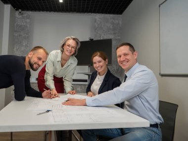 Tasarımcılar bir toplantıda çizimleri tartışırlar. Dört gülümseyen iş adamı kameraya bakıyor.