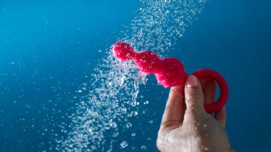 Mavi arka planda akan suyun altında pembe anal boncuklar tutan bir kadın. Seks oyuncağı hijyen konsepti