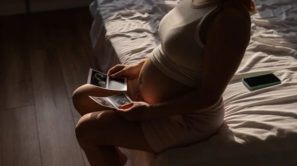 Μια Έγκυος Γυναίκα Κοιτάζει Μια Φωτογραφία Από Έναν Υπέρηχο Ενώ — Φωτογραφία Αρχείου