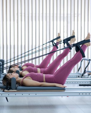 Pembe spor kıyafetli üç Asyalı kadın ıslah yatağıyla pilates egzersizi yapıyor.