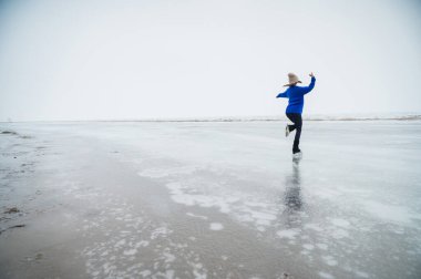 Caucasian woman in a blue sweater skating on a frozen lake