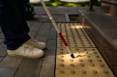 Dokunsal bir değnekle ve engeli gösteren dokunsal bir dokunuşla bir kadının ayaklarının yakın çekimi.