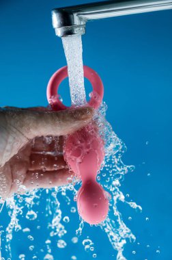 Mavi arka planda akan suyun altında pembe anal boncuklar tutan bir kadın. Seks oyuncağı hijyen konsepti