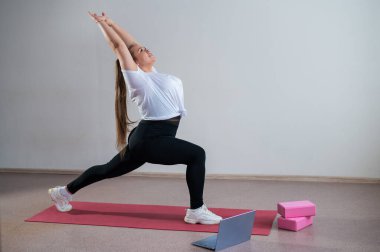 Genç Artı Boyutlu Kadın İnternet 'te esniyor. Esnek kız yoga yapıyor ve internetten dizüstü bilgisayarda ders izliyor..