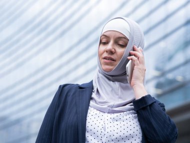 Başörtülü ve takım elbiseli iş kadını akıllı telefondan konuşuyor.