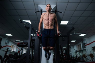 Shirtless man doing triceps dips from parallel bars in gym