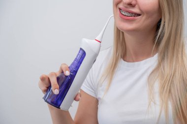 Cropped portrait of a caucasian woman with braces on her teeth holding an irrigator