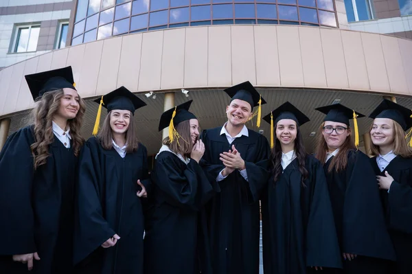 穿着研究生礼服的快乐学生在大学的背景下排成一排 — 图库照片