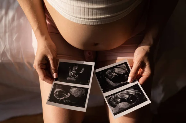 妊娠中の女性はベッドに座りながら超音波から写真を見ている 妊娠中の女性の腹のクローズアップ — ストック写真