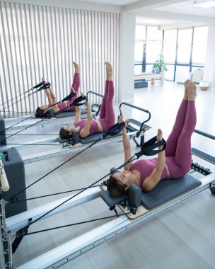Pembe spor kıyafetli üç Asyalı kadın ıslah yatağıyla pilates egzersizi yapıyor.