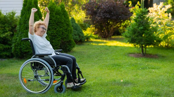 上了年纪的妇女坐在轮椅上散步时伸出手来 — 图库照片