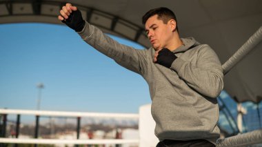 Stadyumda kapüşonlu bir adam boks antrenmanında.