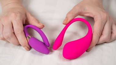 Yatakta uzanmış pembe ve mor vibratörler tutan bir kadın.