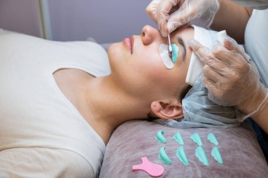 Usta, müşterilerin kirpiklerindeki katman bileşimini pamuklu bezle temizliyor. Kirpik perma prosedürü