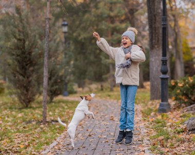 Beyaz kız sonbahar parkında bir köpekle yürüyüşe çıkıyor.