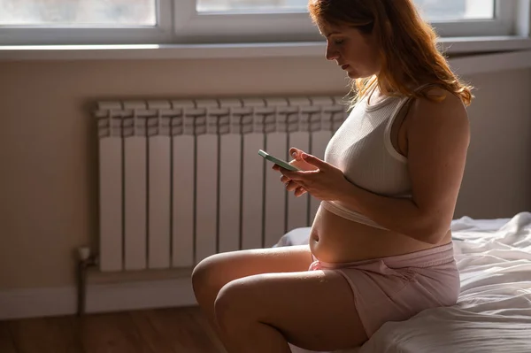 Hamile Bir Kadın Yatakta Otururken Akıllı Telefon Kullanır — Stok fotoğraf