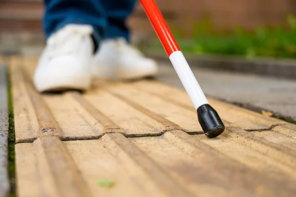 stock image A blind woman walks on the street on tactile yellow tiles. Focus on the tactile cane