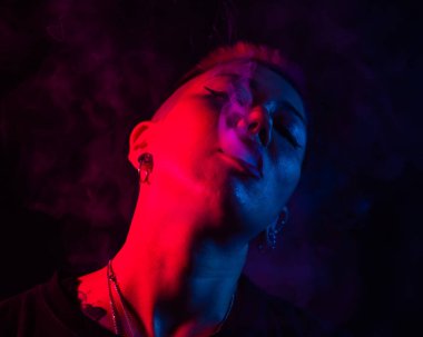 Kısa saçlı, neon ışıkta sigara içen Asyalı kadının yakın portresi.