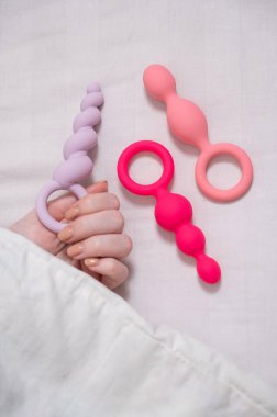 Bir kadın yatakta yatarken bir setten anal boncuk seçer.