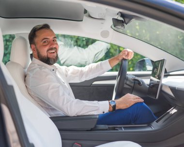 Takım elbiseli beyaz sakallı adam araba kullanıyor.