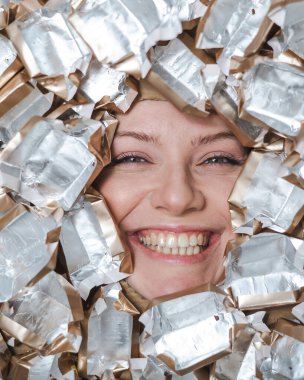 The face of a Caucasian woman surrounded by candy wrappers