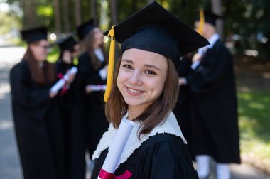 Group of happy students in graduation gowns outdoors. A young girl is happy to receive her diploma