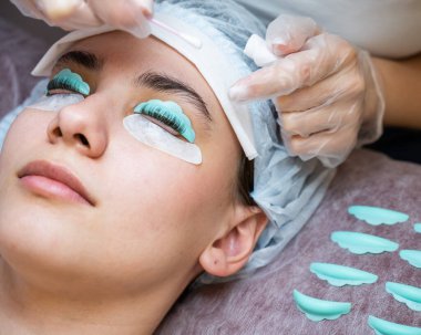 Usta, müşterilerin kirpiklerindeki katman bileşimini pamuklu bezle temizliyor. Kirpik perma prosedürü