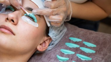 Usta, müşterilerin kirpiklerindeki katman bileşimini pamuklu bezle temizliyor. Kirpik perma prosedürü