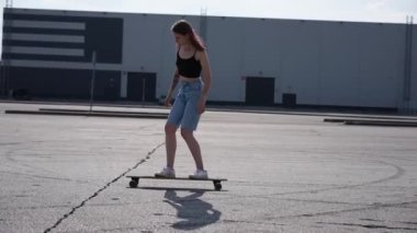 Beyaz bir kadın dışarıda uzun bir sörf tahtasına biniyor. Yavaş çekim