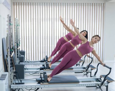 Pembe spor giysili üç Asyalı kadın bir reformcuda yan tahtalar yapıyor. Pilates dersleri