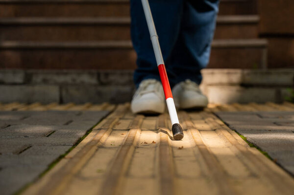 A blind woman walks outdoors using a cane along a tactile yellow tile