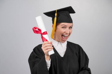 Mezuniyet elbisesi giymiş, ön planda diploması olan duygusal bir kadın.