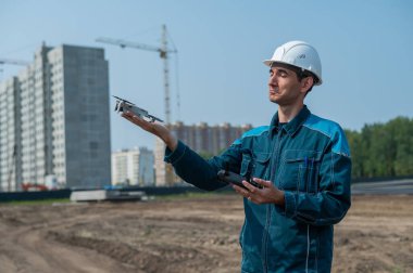 Kasklı ve tulumlu bir adam inşaat alanındaki bir dronu kontrol ediyor. İnşaatçı teknik bir hata yapıyor.