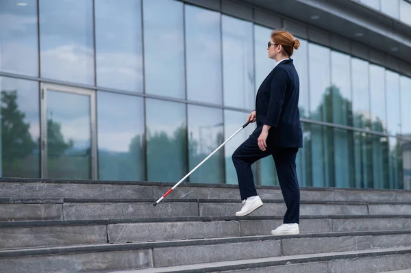 stock image Blind business woman in glasses and with a cane climbs the stairs to the business center