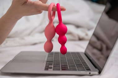 Yatakta yatarken dizüstü bilgisayarın yanında anal boncuk tutan bir kadın.