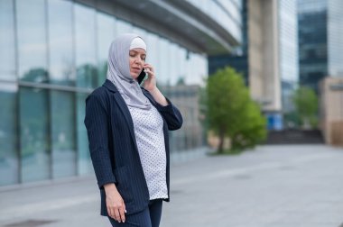 Başörtülü ve takım elbiseli iş kadını akıllı telefondan konuşuyor.
