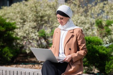 Açık havada dizüstü bilgisayar kullanan tesettürlü genç bir kadının portresi