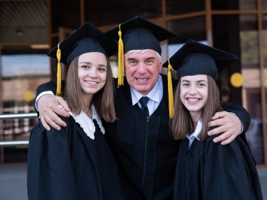 Yaşlı bir adam genç kızlara sarılır. Mezuniyet elbisesi giymiş sınıf arkadaşları.