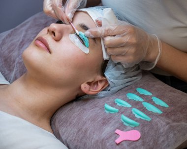 Usta, müşterilerin kirpiklerindeki katman bileşimini pamuklu bezle temizliyor. Kirpik perma prosedürü