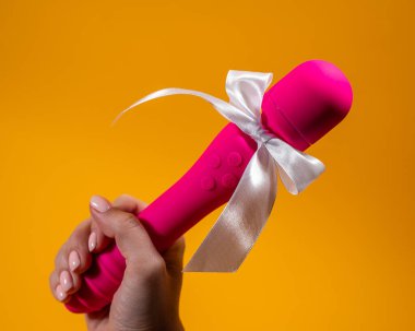 Elinde pembe vibratör, turuncu arka planda beyaz fiyonklu bir kadın.