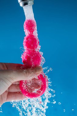 Mavi arka planda akan suyun altında pembe anal boncuklar tutan bir kadın. Seks oyuncağı hijyen konsepti