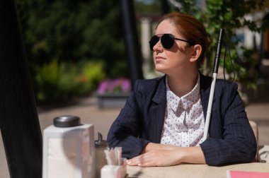 Takım elbiseli kör bir kadın açık bir kafede oturuyor.