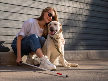 Kör bir kadın rehber köpeğini sokakta gezdirir. Labradora sarılan kız