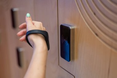 Bir kadın soyunma odasındaki kabinin elektronik kilidini bileziğiyle açıyor.