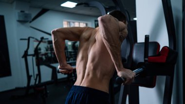 Shirtless man doing triceps dips from parallel bars in gym