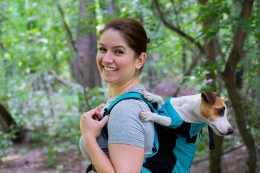 Beyaz bir kadın özel bir sırt çantasıyla köpek Jack Russell Terrier ile dışarı çıkıyor.