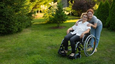 Beyaz bir kadın tekerlekli sandalyede oturan yaşlı bir anneye sarılıyor. Dışarı çık.